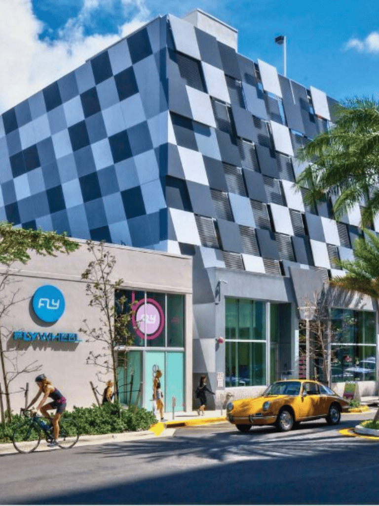 Modern mixed-use building with retail storefronts, pedestrians, and a yellow vintage car in a vibrant urban setting.