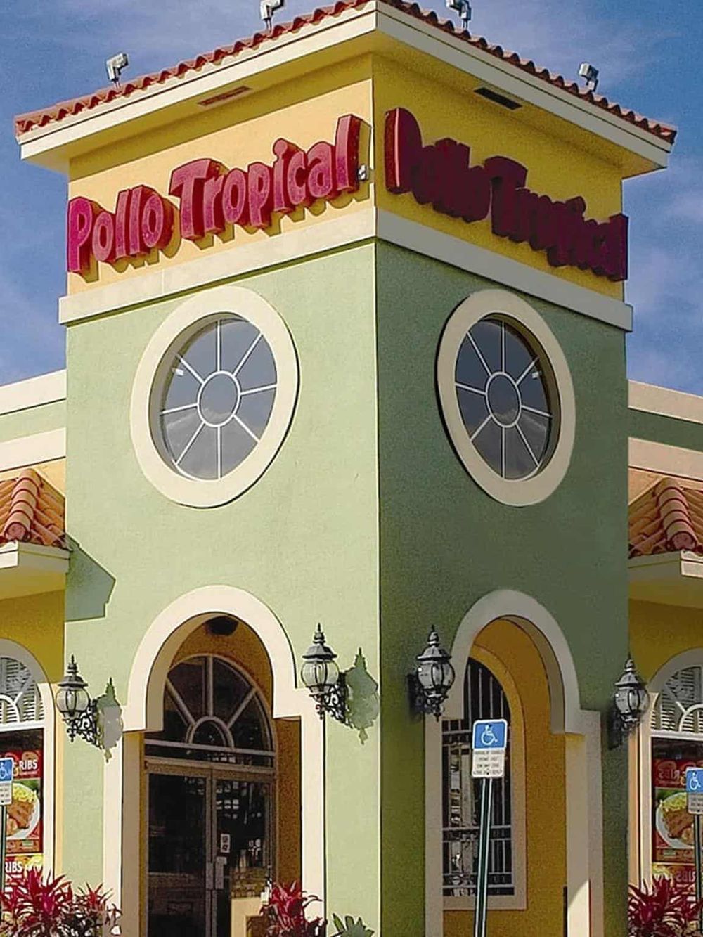 Bright colorful restaurant exterior with "Pollo Tropical" sign and Spanish-style architecture, sunny day.