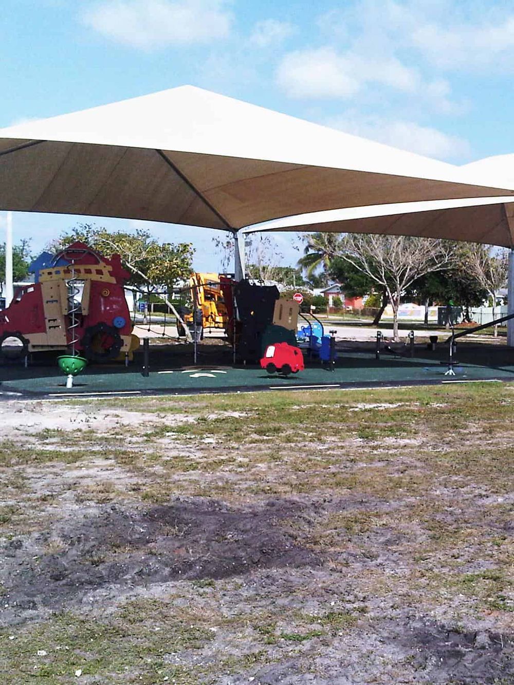 Colorful playground equipment under a beige canopy in a sunny outdoor area.