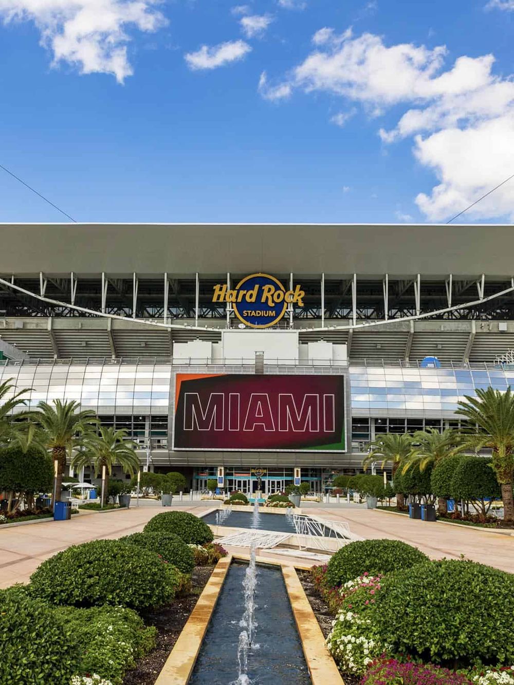 Miami sports stadium entrance with palm trees and water fountain, home of Hard Rock Stadium.