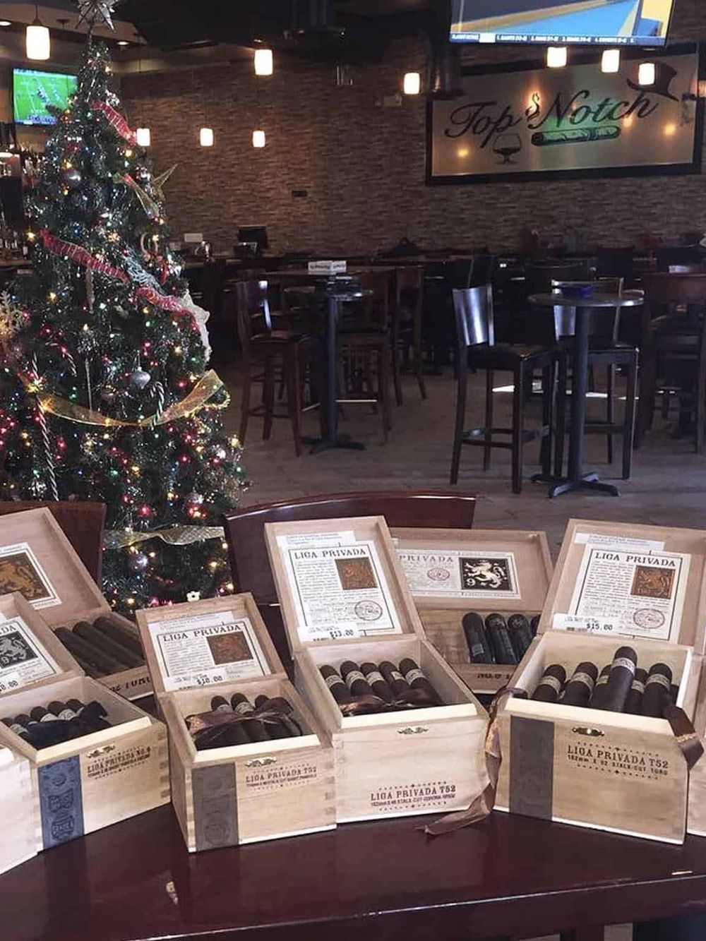 Luxurious cigars in open wooden boxes at a cozy bar decorated for Christmas with a Christmas tree.