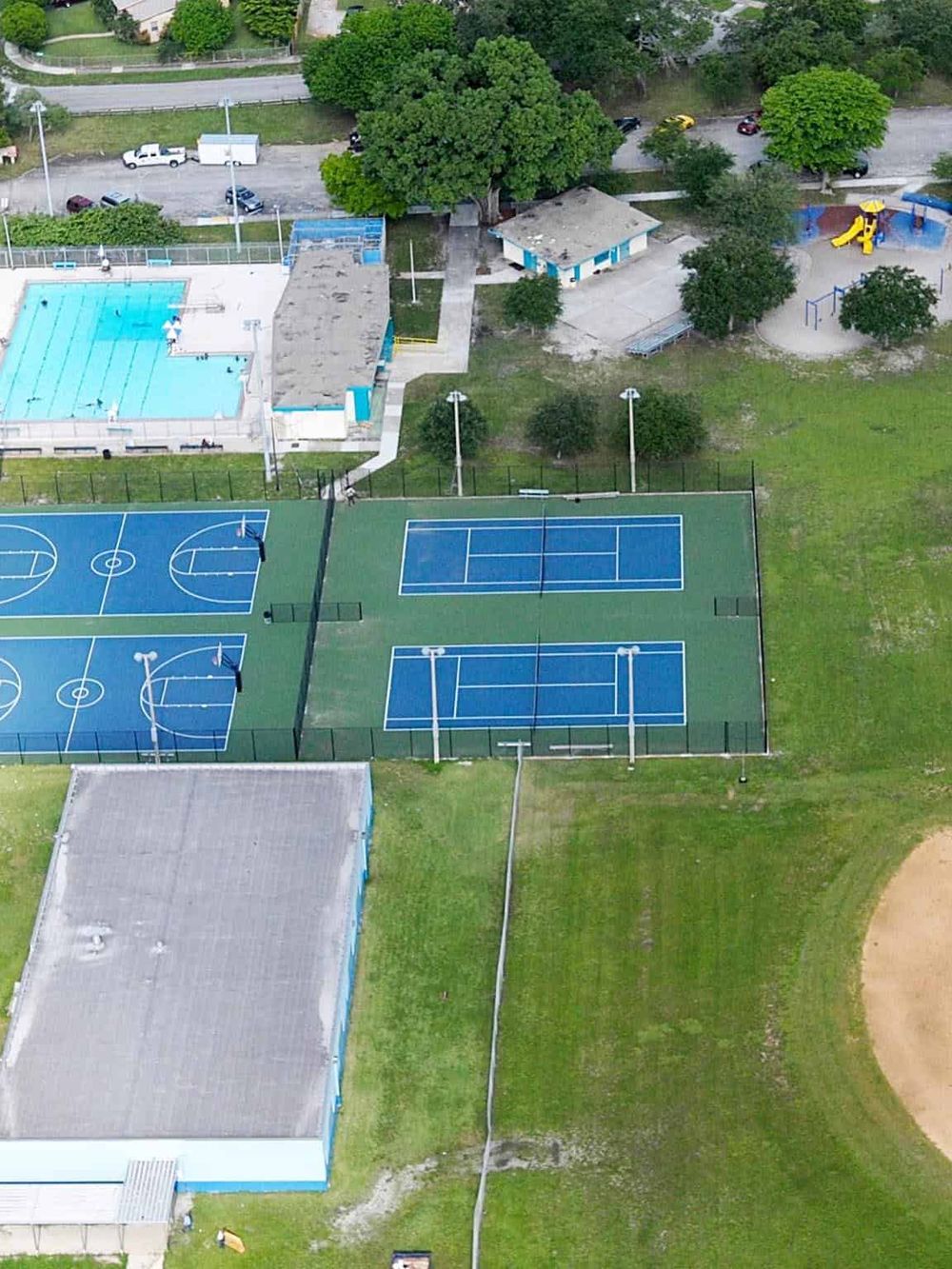 Basketball and tennis courts in a community park with playground nearby, outdoor sports facilities, and trees.