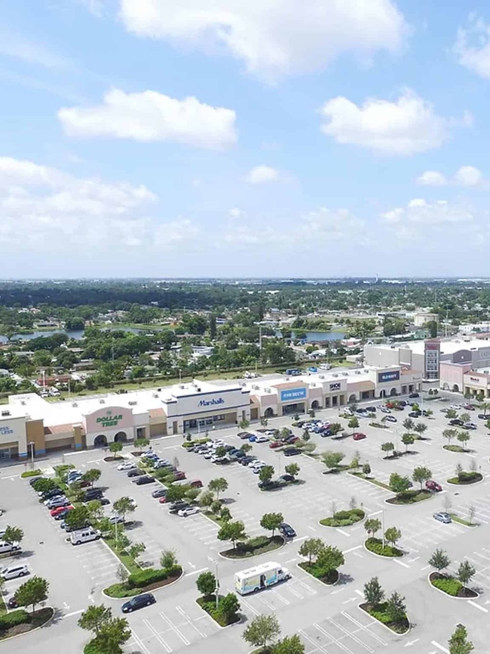 Bright shopping plaza with retail stores and ample parking in a suburban area.