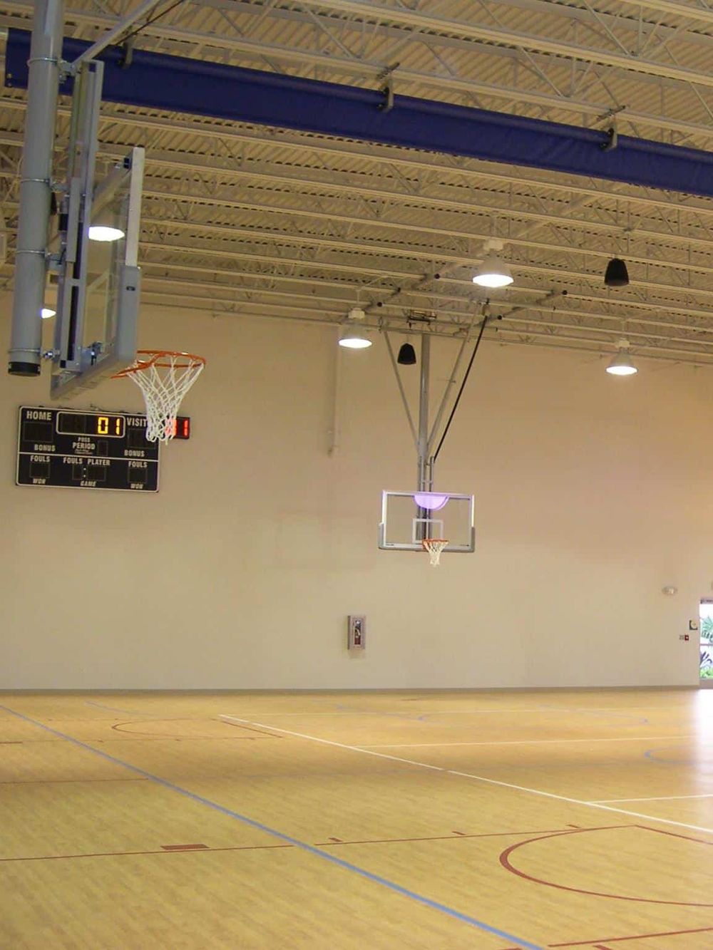 Bright indoor basketball court with multiple hoops and electronic scoreboard for sports activities and player directions.