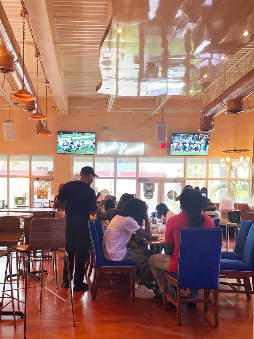 Cozy restaurant interior with customers enjoying sports on multiple TV screens, vibrant atmosphere, and modern decor.
