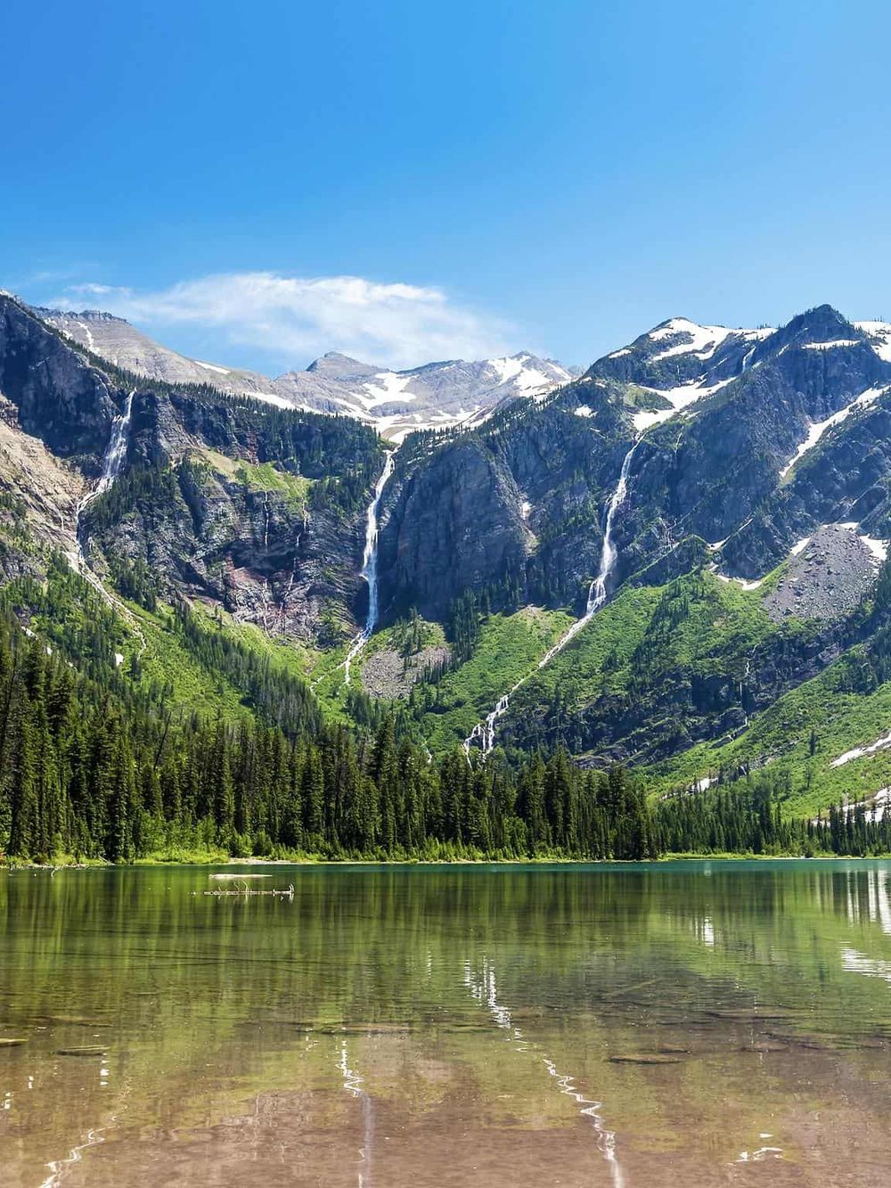 Stunning mountain landscape with waterfalls and lush green forest near a calm lake.