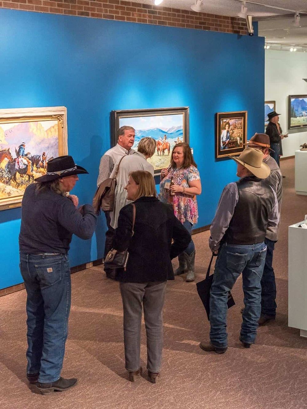 People viewing art at an art gallery or museum, engaging in conversation and appreciating landscape paintings.