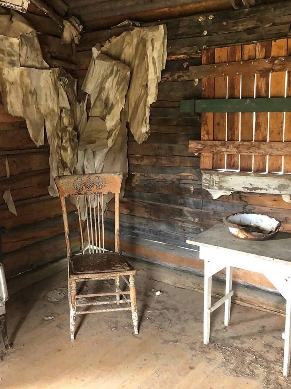 Weathered wooden chair in rustic cabin interior with peeling wall coverings and vintage decor.