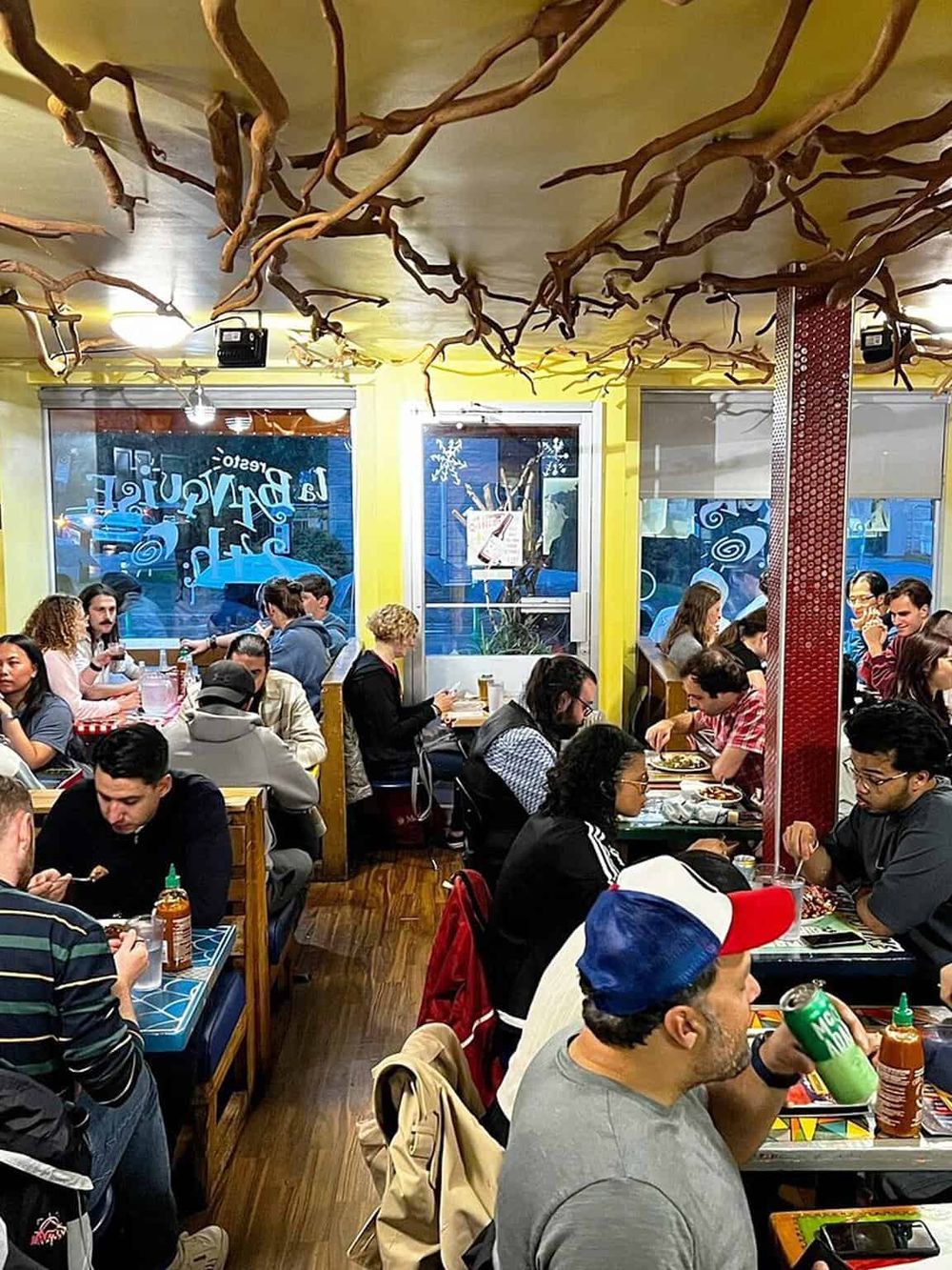 Colorful restaurant interior with diverse diners, vibrant decor, and unique ceiling design featuring twisted branches.