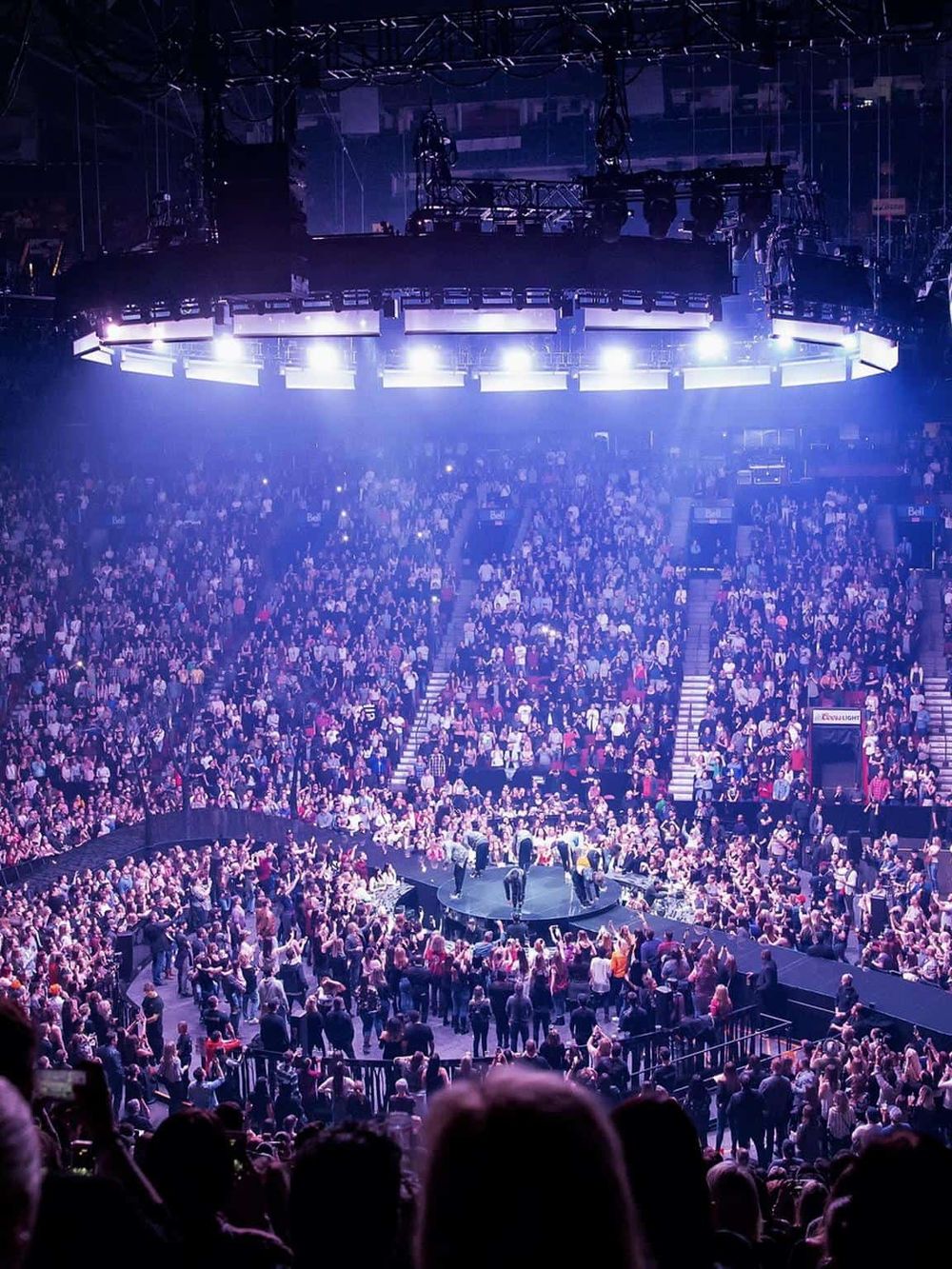 Bright arena with large audience watching a mixed martial arts event, illuminated by intense overhead lighting.