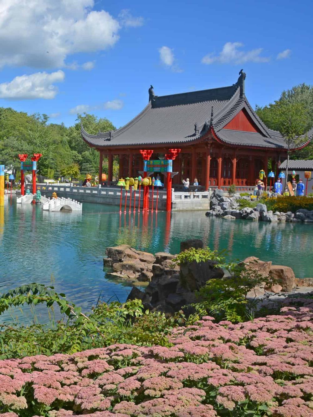 Serene Chinese garden with traditional pavilion, bright red lanterns, garden pond, lush greenery, and colorful flowers, ideal for sightseeing and relaxation.