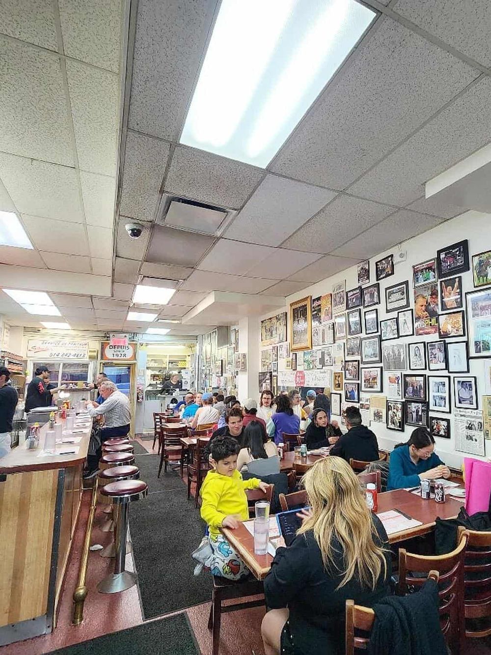Cozy New York City restaurant interior with patrons enjoying meals, decorative framed photos on the wall.