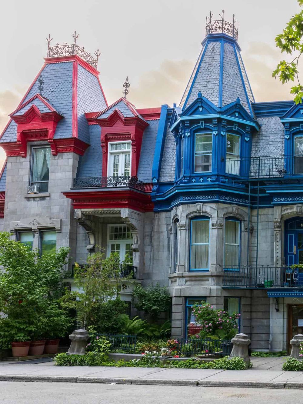 Colorful Victorian mansion with blue and red accents, lush greenery, and intricate architectural details.