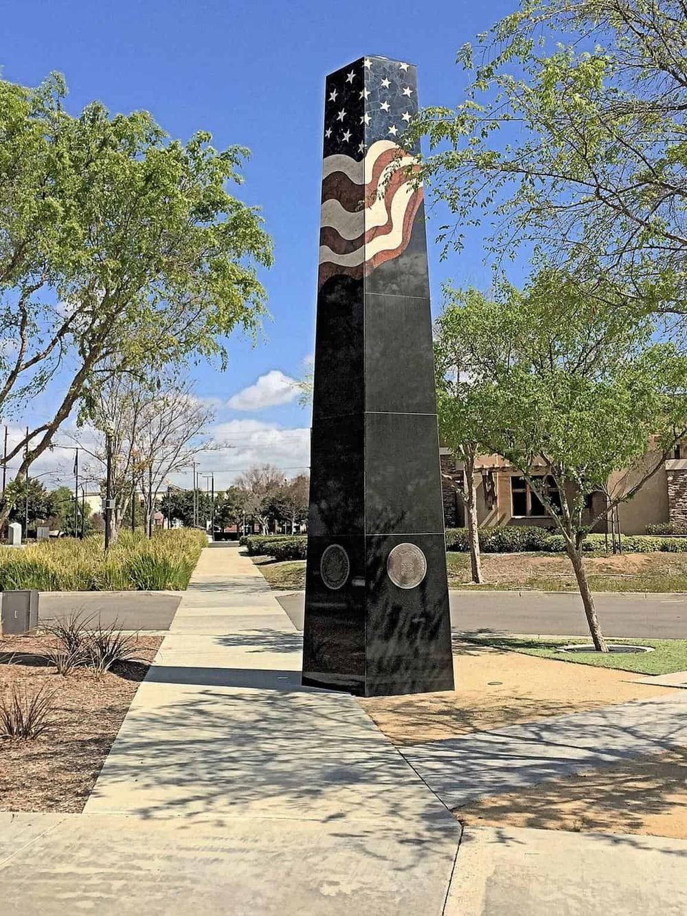 American flag sculpture on black granite monument with courthouse and trees in background.