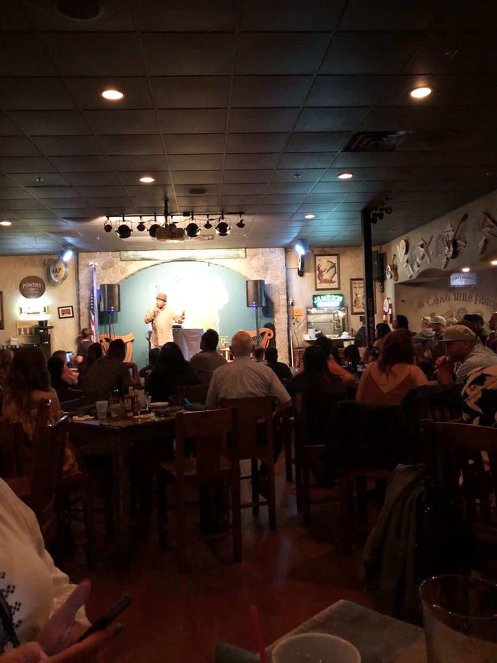A lively indoor comedy show at a restaurant or bar with an audience watching a performer on stage.