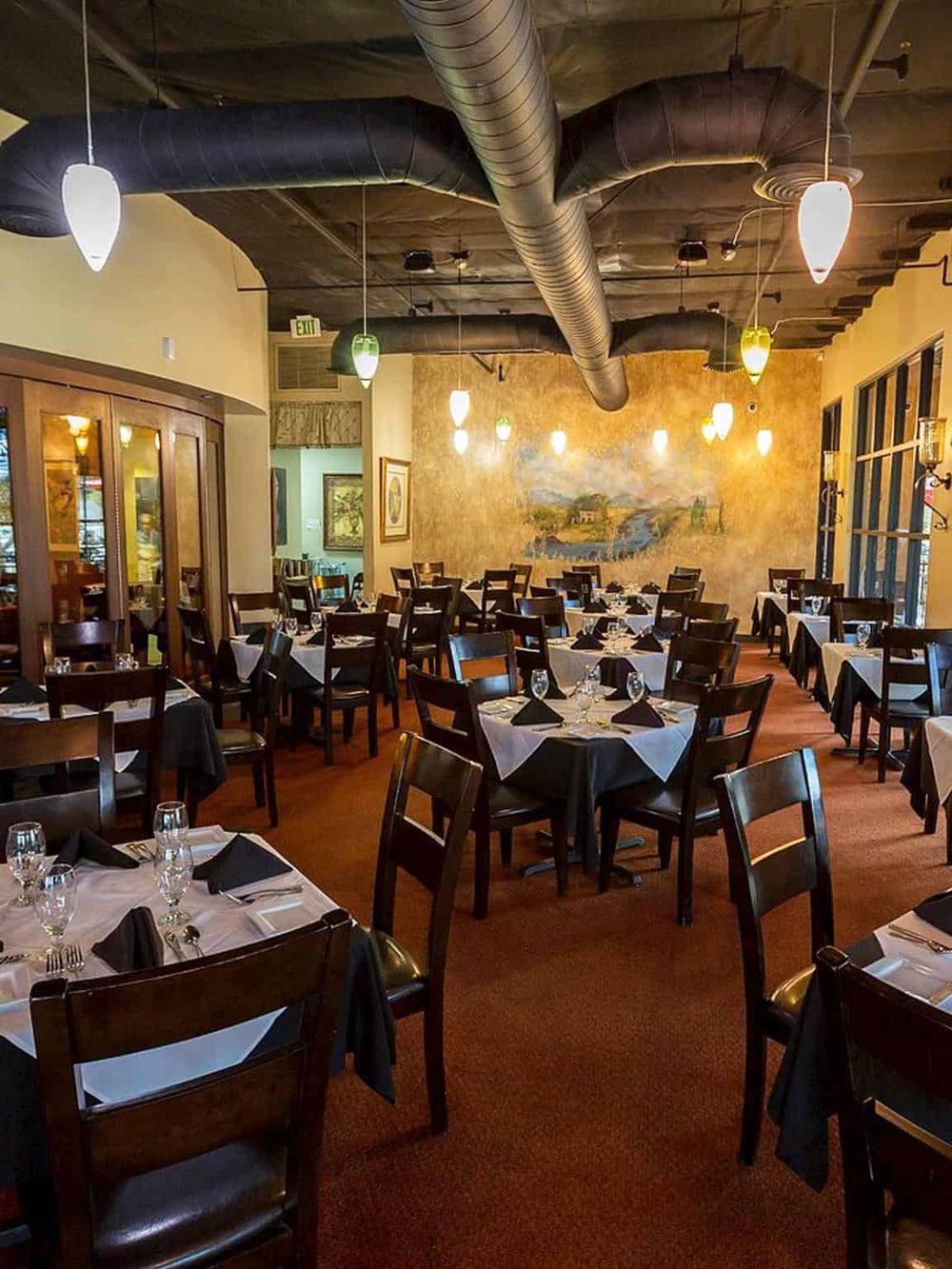 Elegant restaurant interior with black and white table settings, warm lighting, and artistic decor.