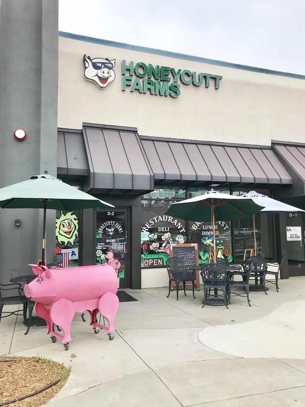 Colorful farm-themed restaurant exterior with signage, pink pig cart, outdoor seating, and playful décor at Honeycutt Farms.