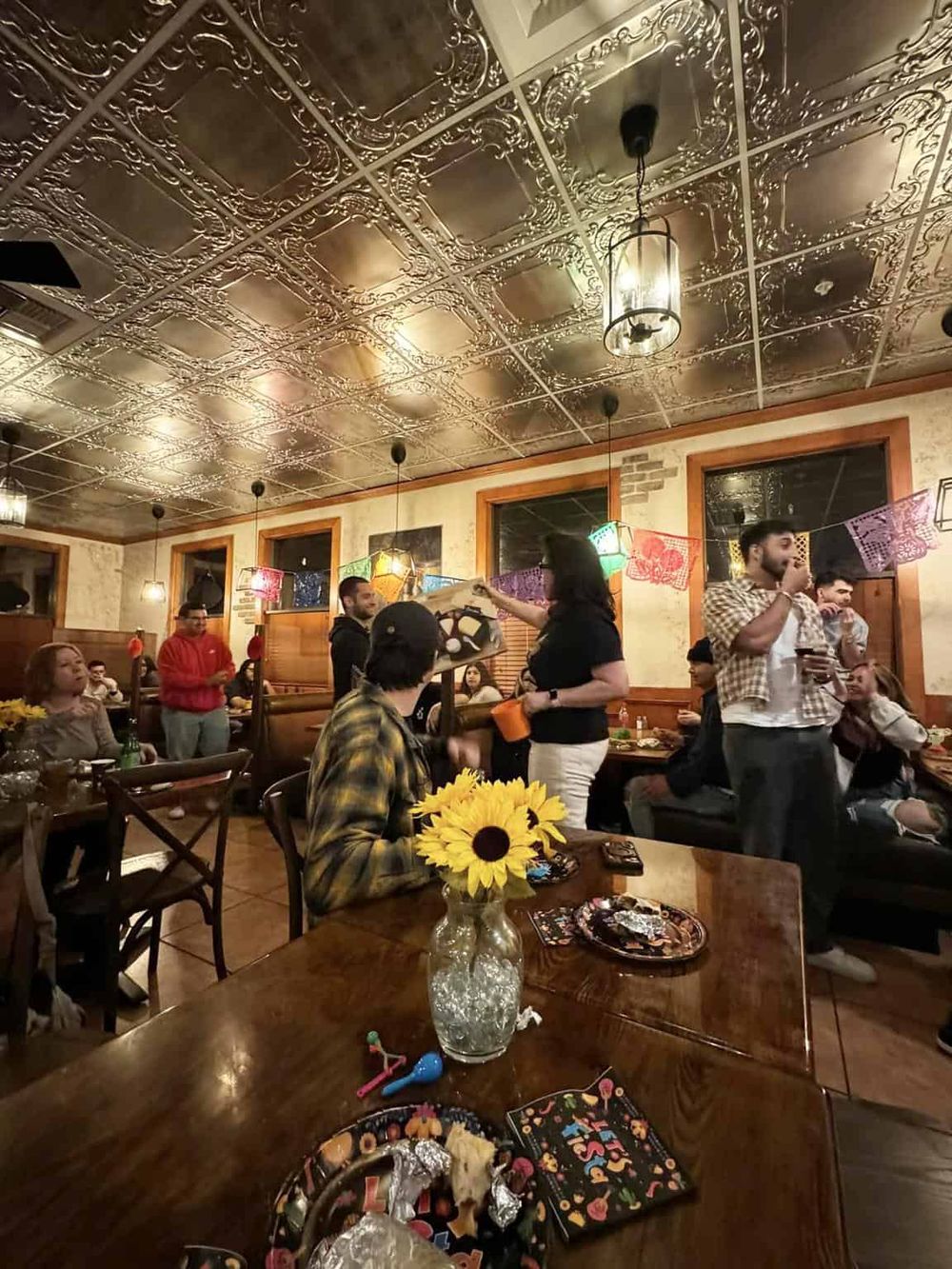 Colorful fiesta decorations at a lively Mexican restaurant with customers enjoying food and drinks.