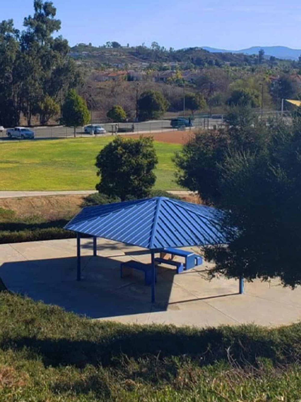 Colorful blue gazebo in a park with surrounding trees and scenic hills, ideal for outdoor navigation and directions.