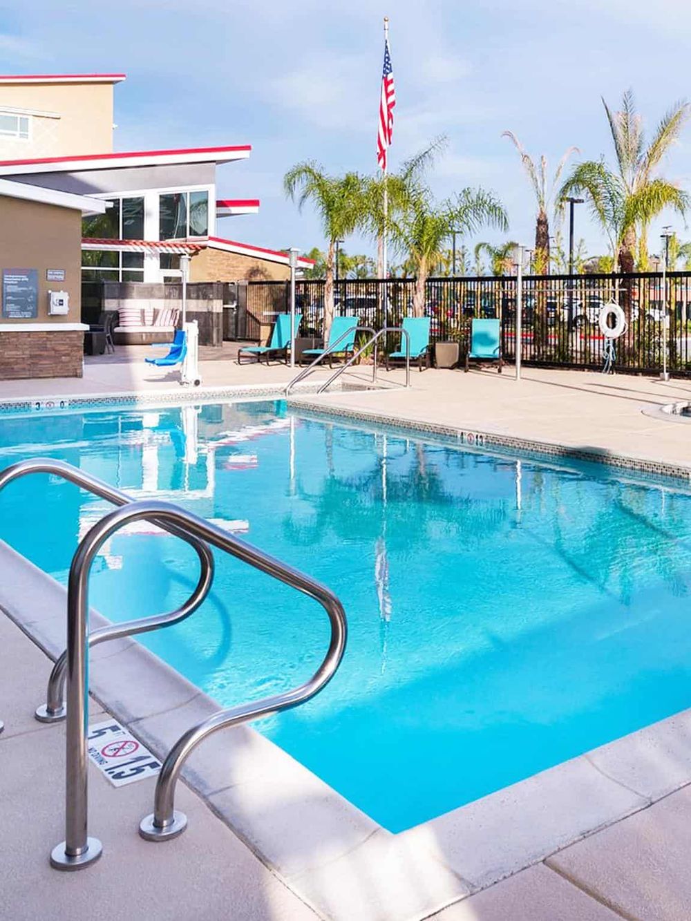 Modern hotel swimming pool with lounge chairs, palm trees, and American flag, ideal for relaxation.