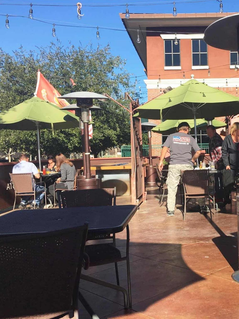Outdoor dining at a casual restaurant with green umbrellas and string lights in a sunny setting.