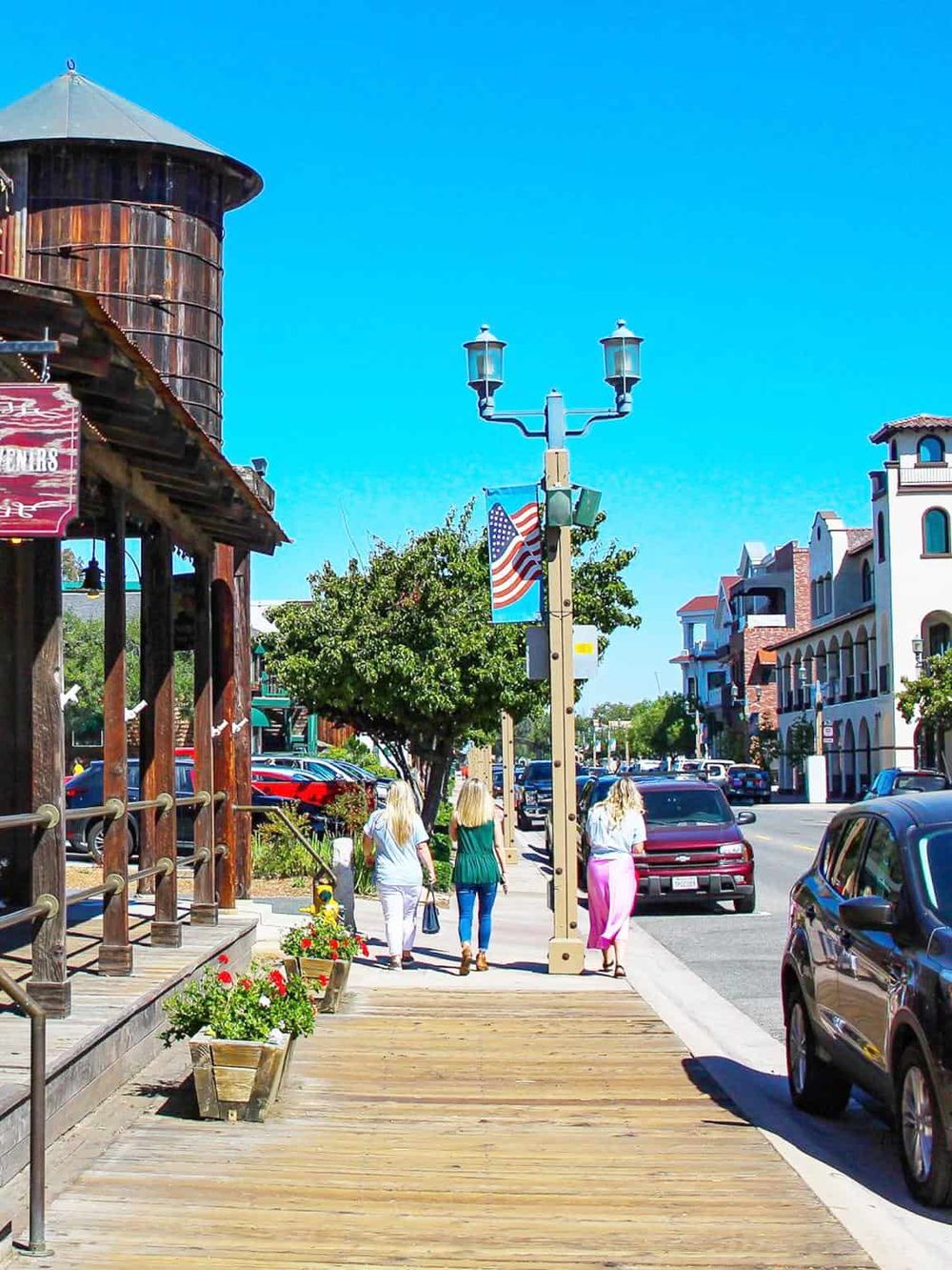 Charming downtown street with shops, pedestrians, and parked cars in a vibrant local shopping district.