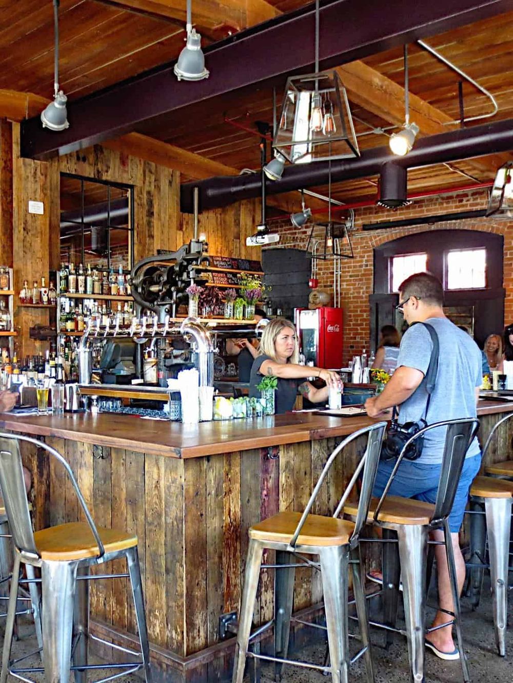 Cozy bar scene in a rustic-style restaurant with wood and brick accents, friendly bartender serving drinks, and guests enjoying their time.