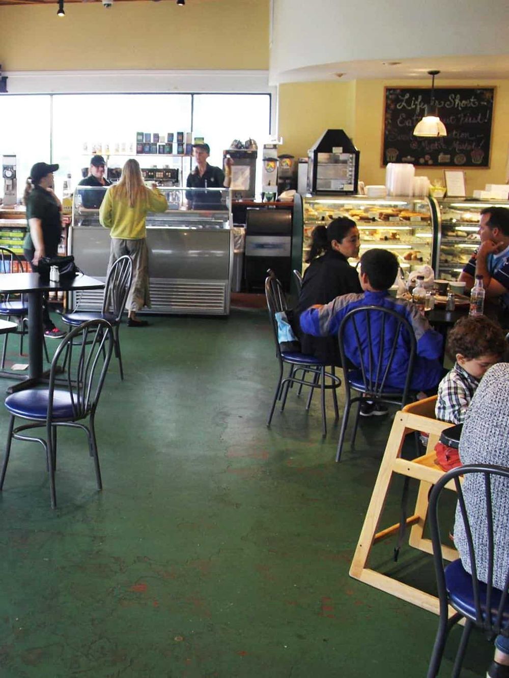 Bright indoor cafe with customers enjoying meals and drinks, high-rise windows, and a welcoming family-friendly atmosphere.