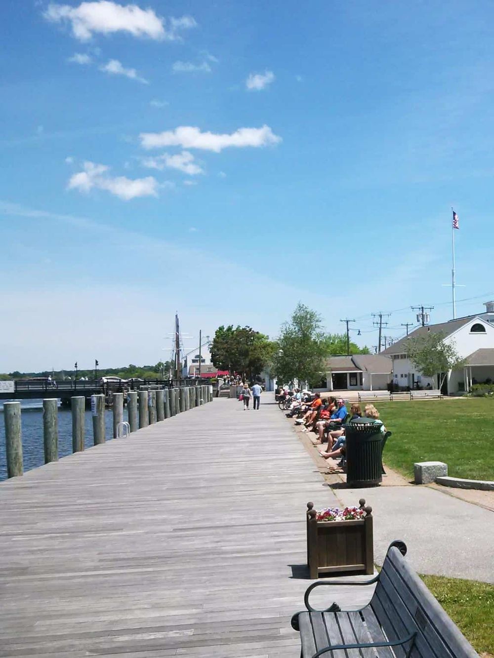 Scenic waterfront boardwalk with benches, shops, and people enjoying a sunny day by the river.