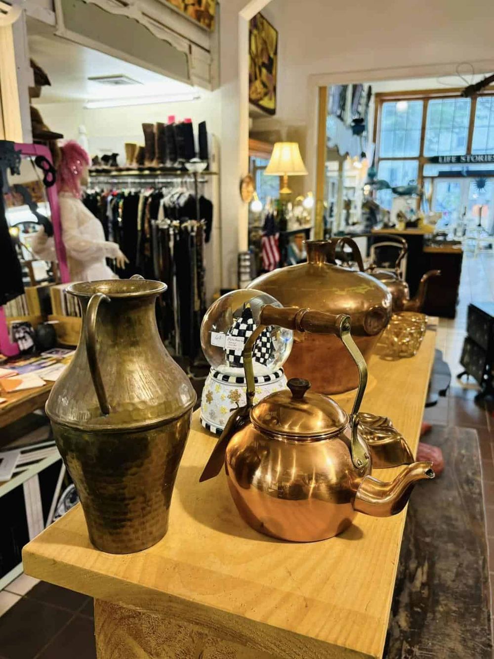 Vintage copper and brass teapots displayed in a charming thrift store or antique shop setting.