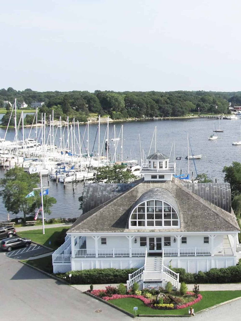 Marina with boats docked at a scenic waterfront, featuring a stylish building with large windows and surrounding landscaped garden.