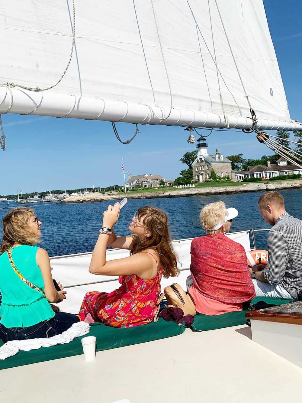 Relaxed group enjoying a boat trip with scenic harbor views and lighthouse in the background, perfect for a memorable outdoor adventure.