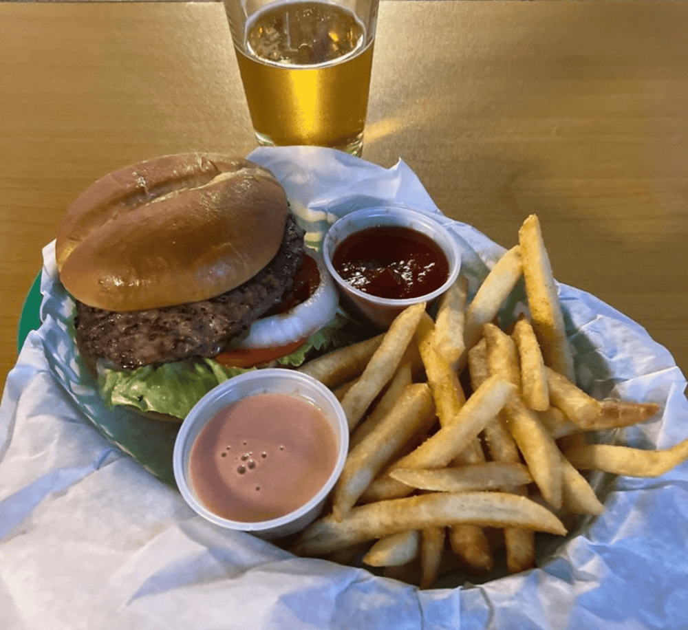 Juicy burger with fries, ketchup, and dipping sauces on a basket at a restaurant.
