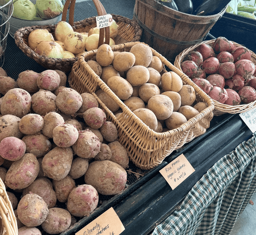 Fresh organic root vegetables at a farmers market, including beets, potatoes, and onions.
