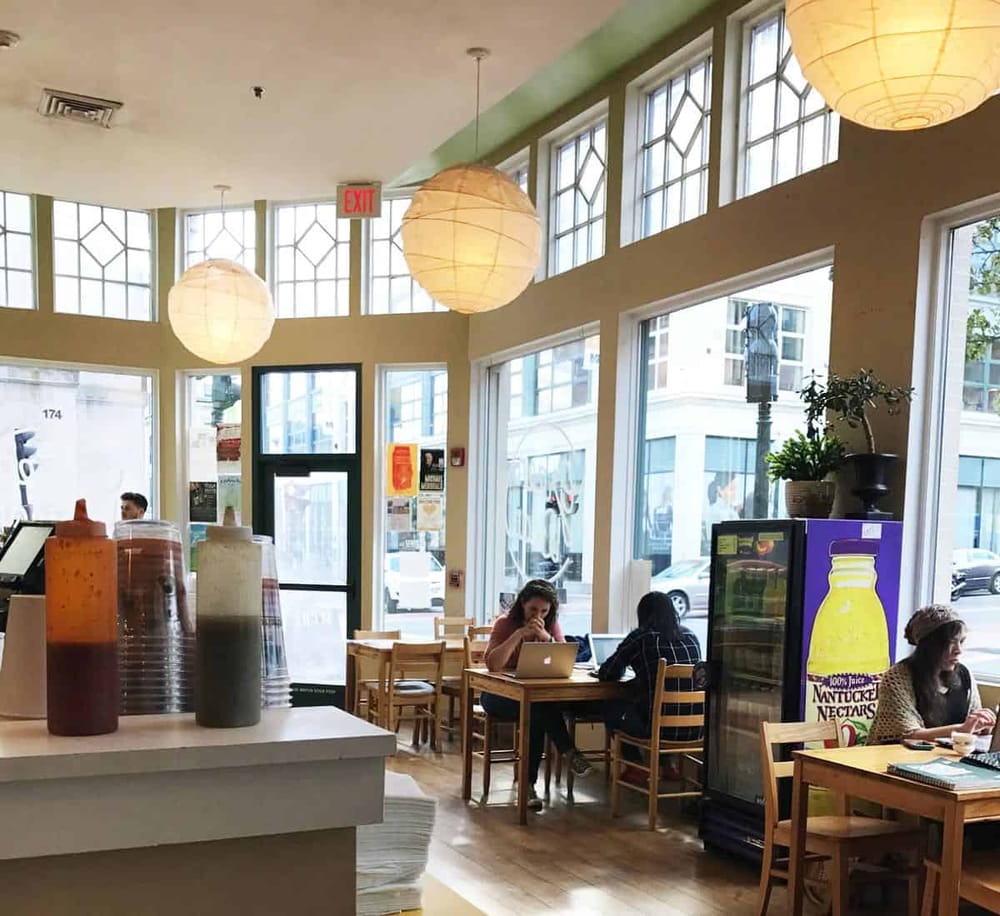 Cozy cafe interior with natural light, wooden tables, and customers working on laptops, perfect for relaxing or remote work.