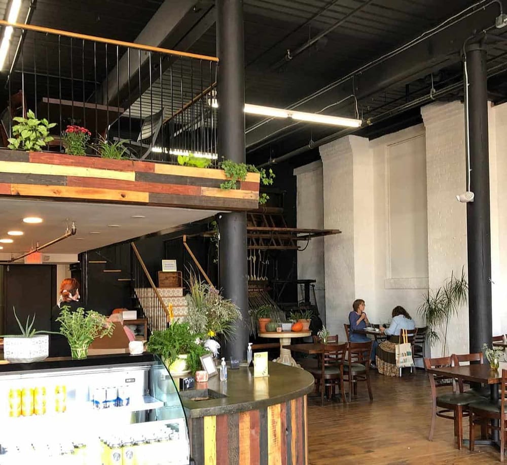 Cozy modern cafe interior with plants, wooden furniture, and a welcoming atmosphere for dining and relaxing.