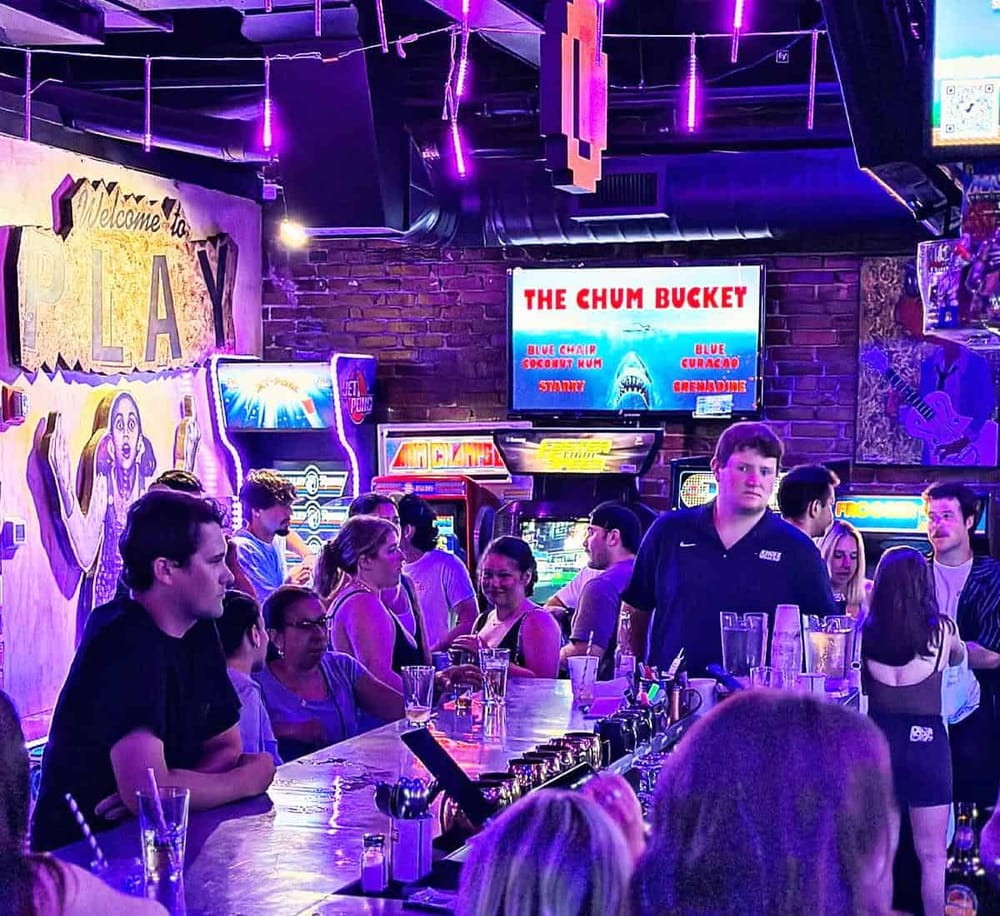 Vibrant arcade bar scene with neon lights, arcade games, and socializing at Quest For Directions.