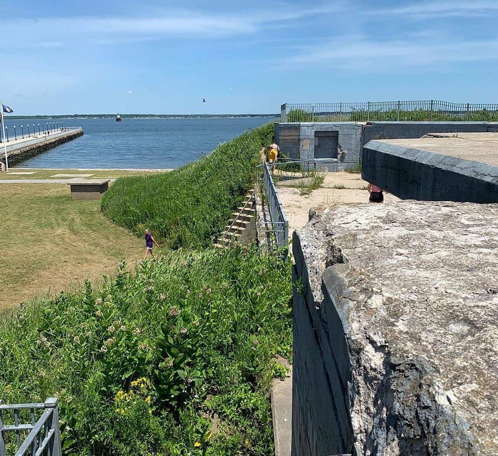 A scenic view of water with a grassy area, stone structures, and visitors exploring coastal history and navigation.