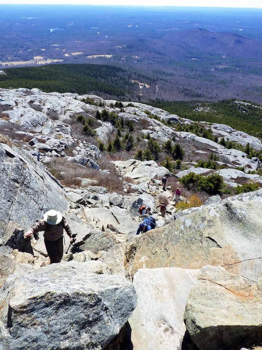 Hiking on rocky mountain trail with scenic view of forest and distant landscape, adventure and nature exploration.