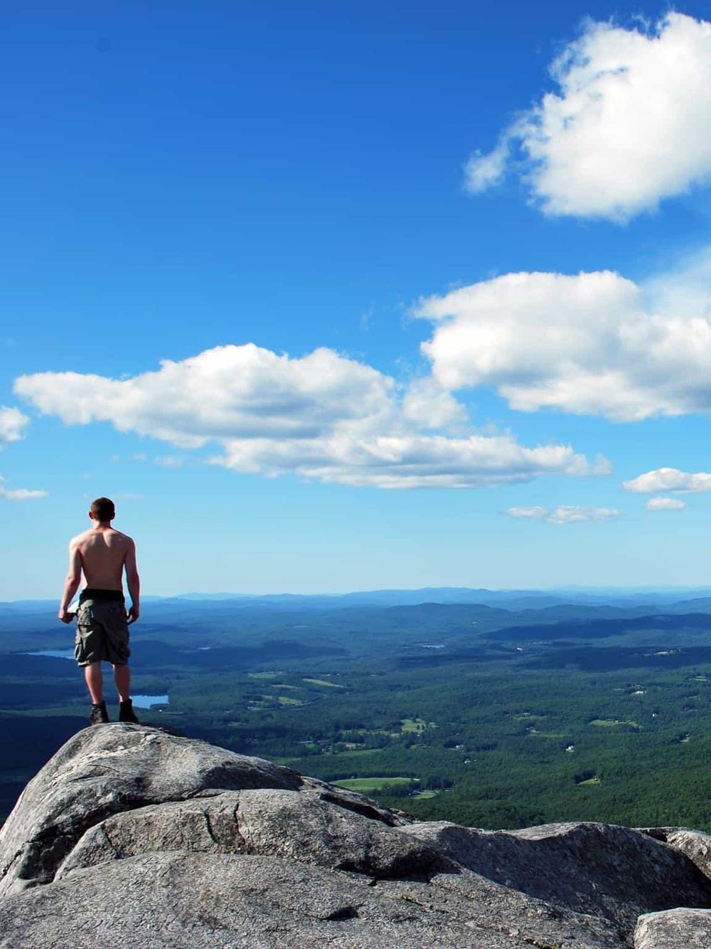 Breathtaking mountain view with a hiker overlooking lush valleys and clear blue skies, perfect for adventure travel and outdoor exploration.