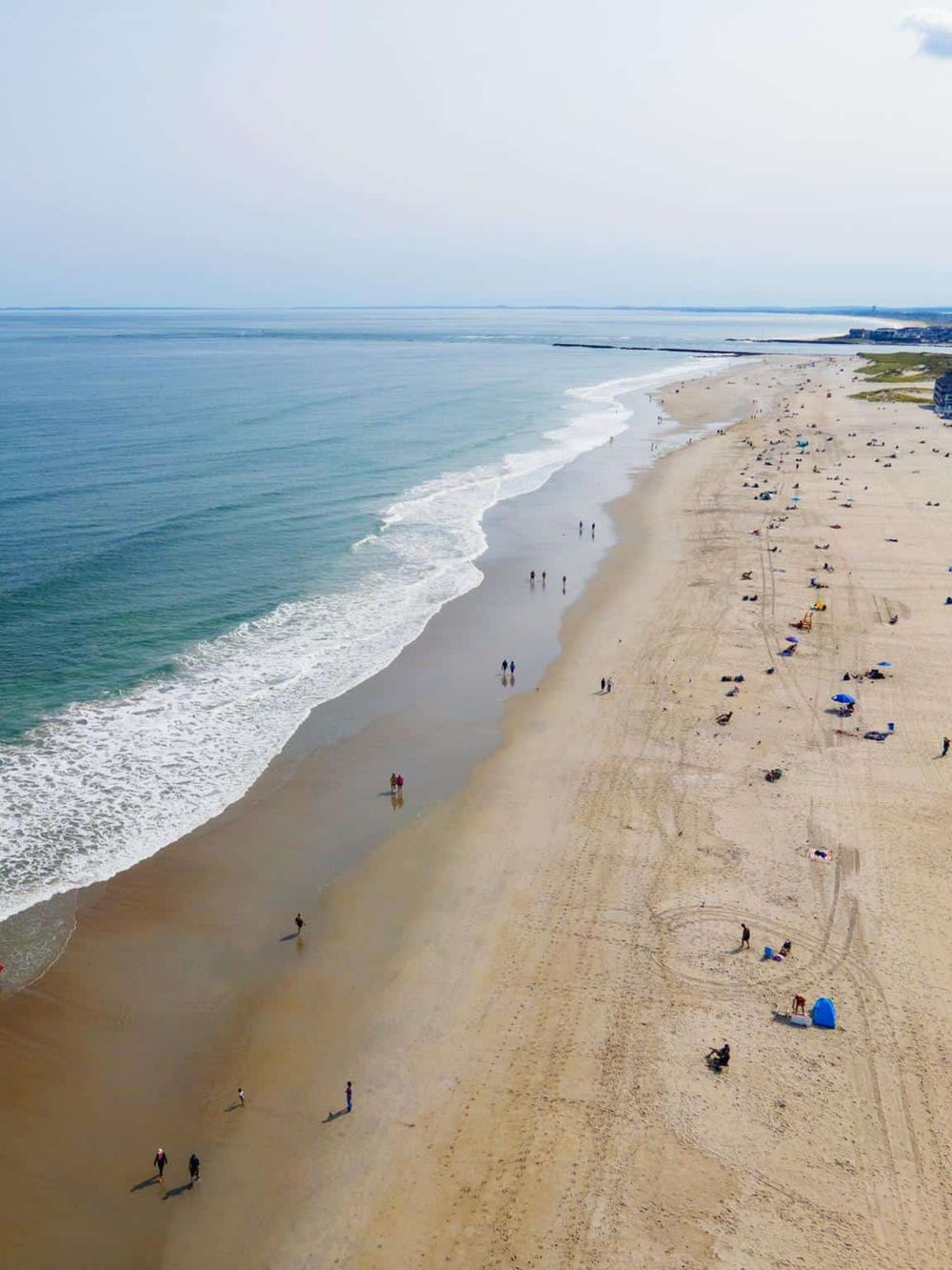 Aerial view of a sandy beach with ocean waves, people relaxing and enjoying the seaside.