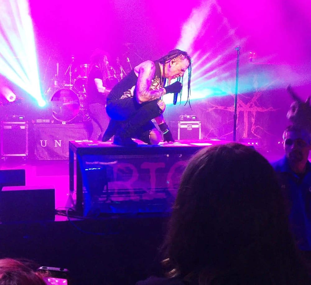 Vivid live music performance with a vocalist kneeling on stage, colorful stage lighting, and energetic atmosphere.