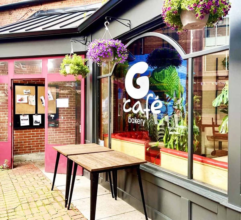 Colorful bakery cafe storefront with hanging flower baskets and outdoor tables, inviting for breakfast and coffee.