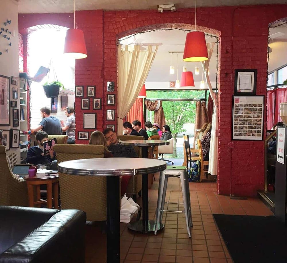 Cozy coffee shop interior with red brick walls, hanging red lamps, and customers enjoying their drinks and conversation.