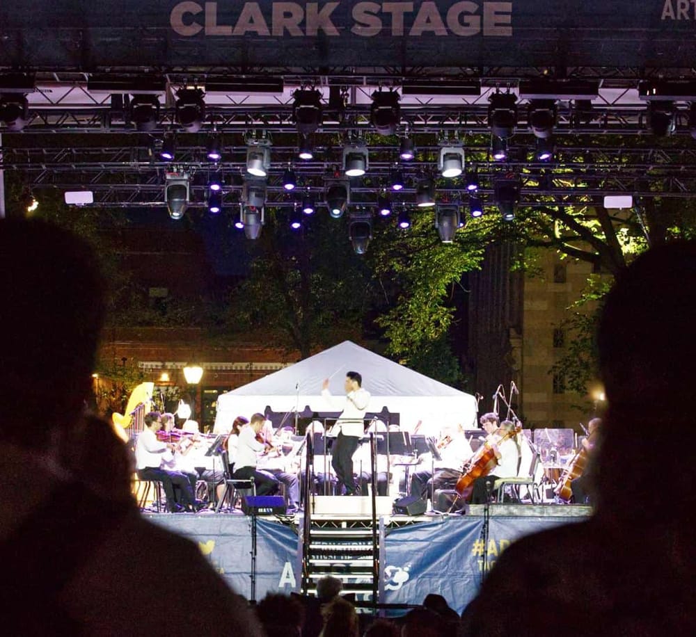 Elegant outdoor symphony concert on Clark Stage with musicians performing at night.