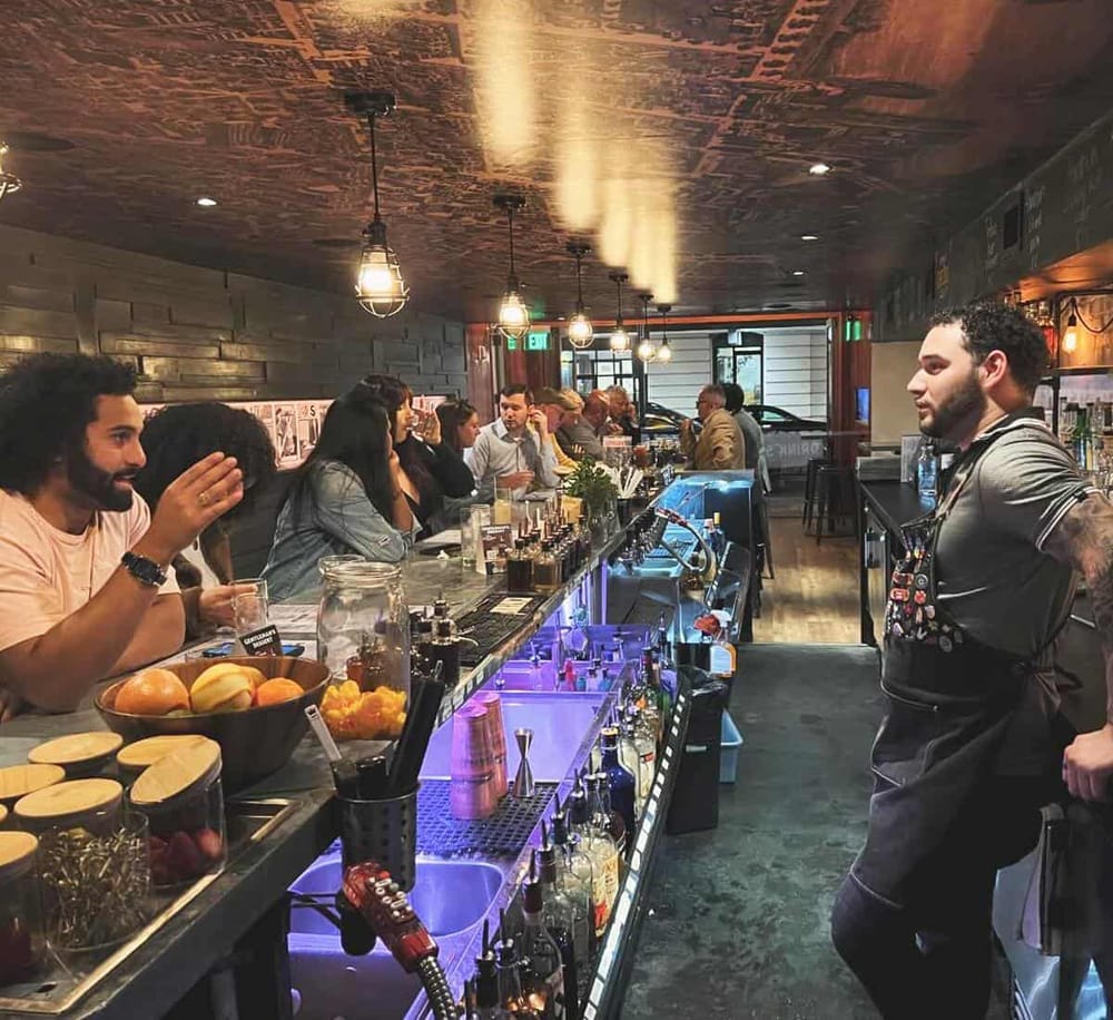 A lively bar scene with diverse patrons enjoying drinks and conversation at a cozy, modern cocktail lounge.