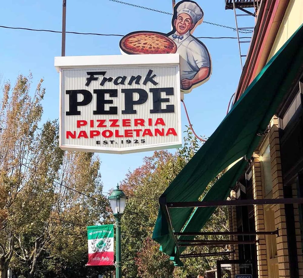 Pizza restaurant sign with cartoon chef, pizza, and tree-lined street scene.