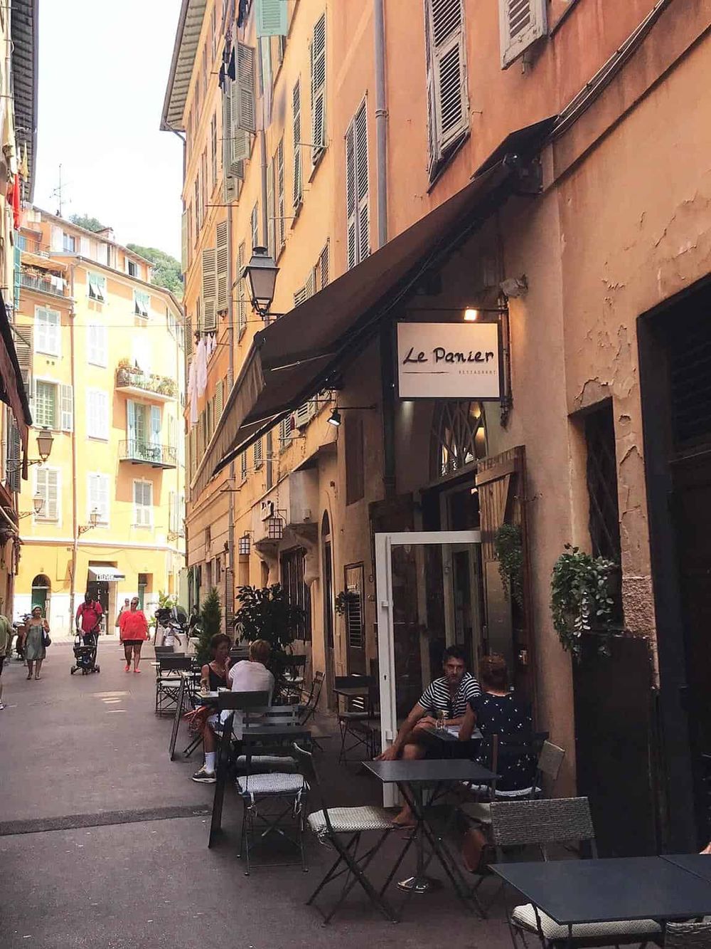 Cozy outdoor dining scene on a charming European alleyway in Nice, France with colorful old buildings.