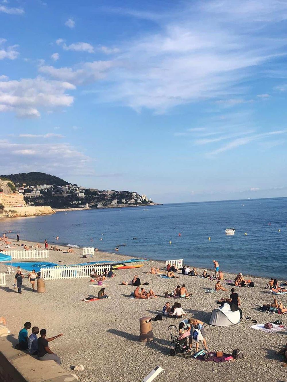 Sunny beach scene with people relaxing, swimming, and enjoying the seaside view.