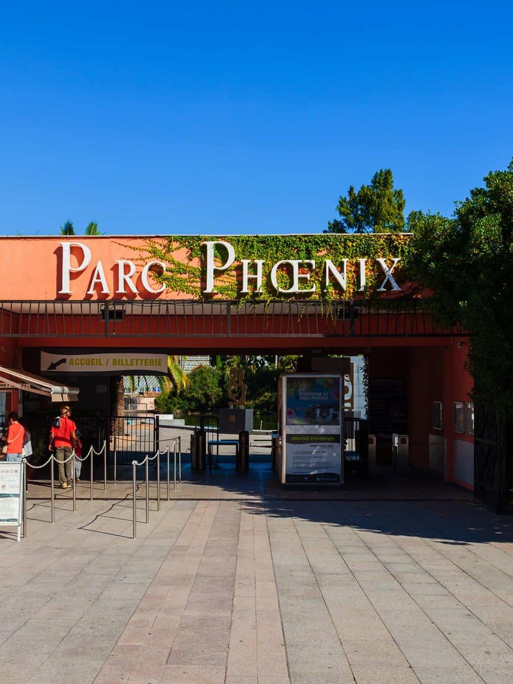 Outdoor entrance to Parc Phoenix botanical gardens and zoo in Nice, France, with visitors and clear signage.